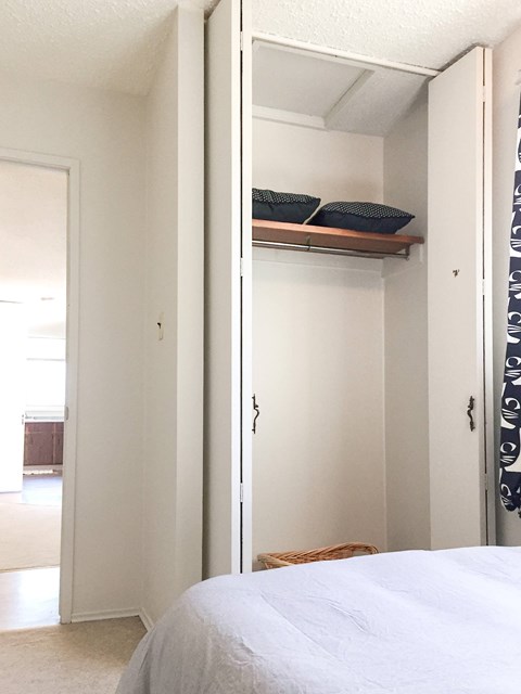 A white bedroom with a bed and a shelf above it.