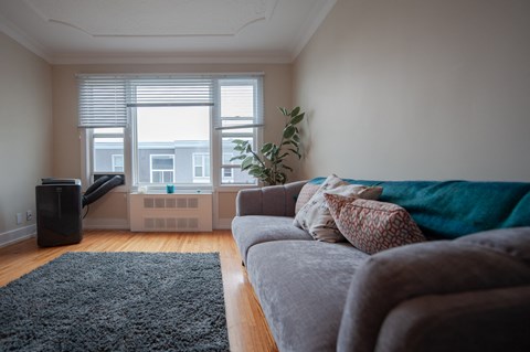 A living room with a grey couch and a black speaker.