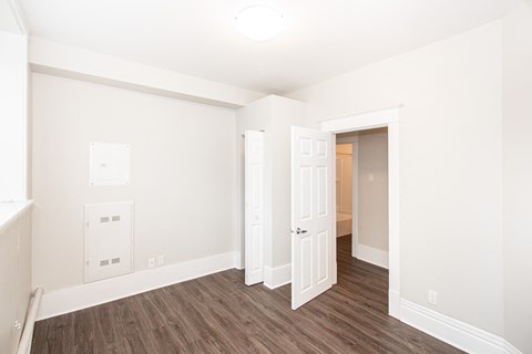 a bedroom with white walls and wood flooring and a closet