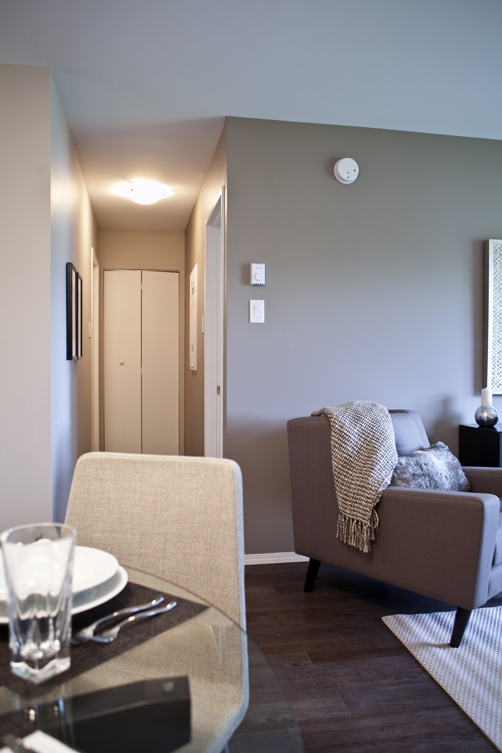 A modern living room with a grey couch, a glass table, and a white chair.
