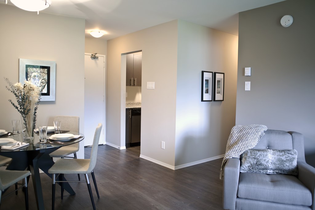 A grey couch with a white blanket is in the corner of a room with a dining table and chairs.