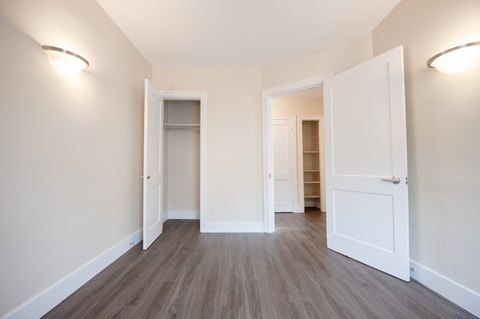 a bedroom with white walls and wood flooring and a closet