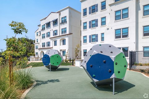 A playground with two large blue and green climbing structures in front of a white building.