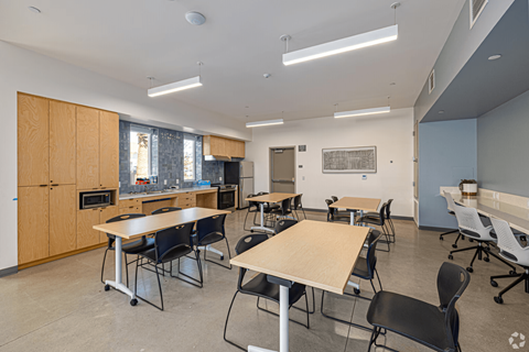 A room with tables and chairs and a kitchen area.