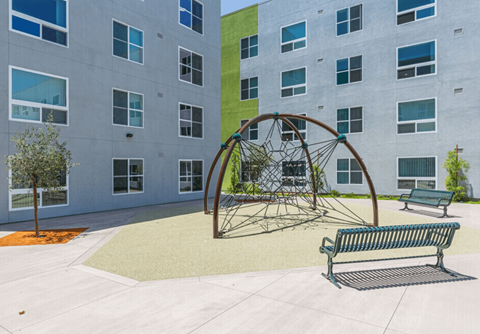 A playground with a swing set and two benches in front of a building.