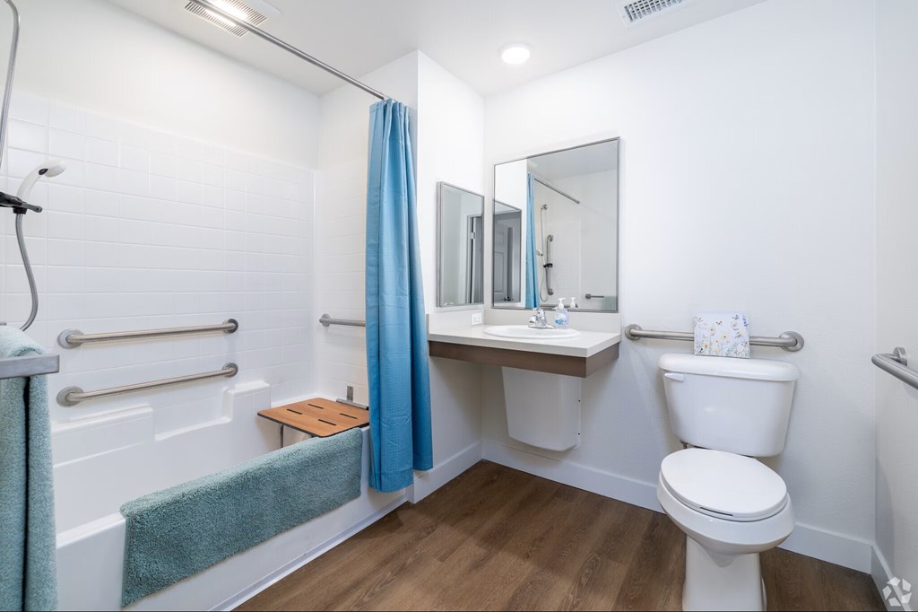 A white bathroom with a white toilet, a sink with a mirror and a blue shower curtain.
