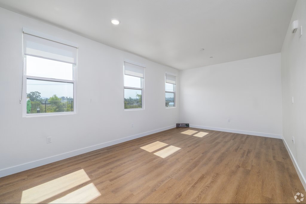 A room with wooden flooring and two windows.