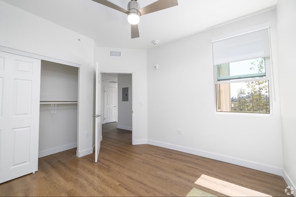 A room with a ceiling fan and a window with a view of trees.