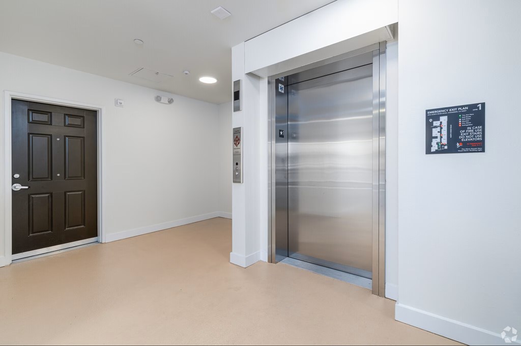 A room with a brown door and a stainless steel elevator.