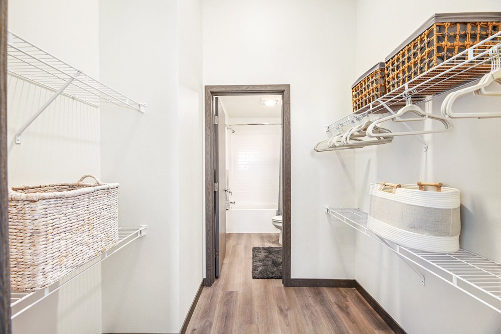 a walk in closet with white walls and shelves and a door to a bathroom