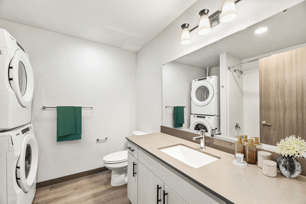 a white bathroom with a washer and dryer and a sink and a mirror
