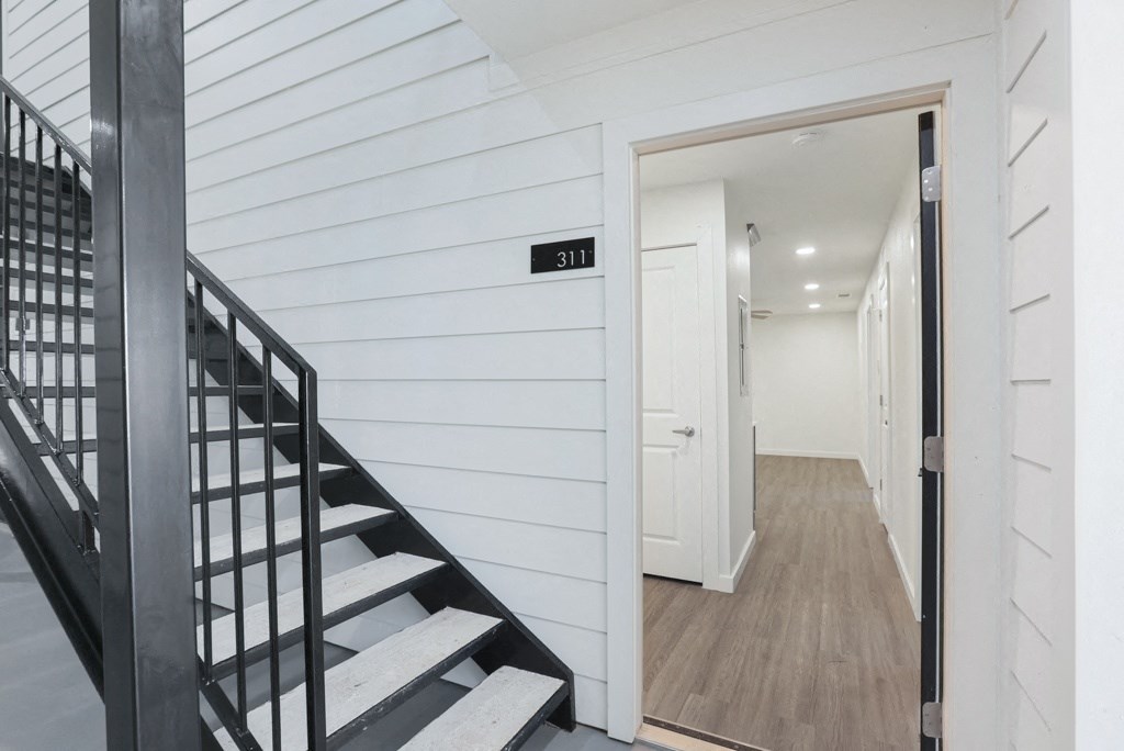 a hallway with white walls and a staircase with black railings