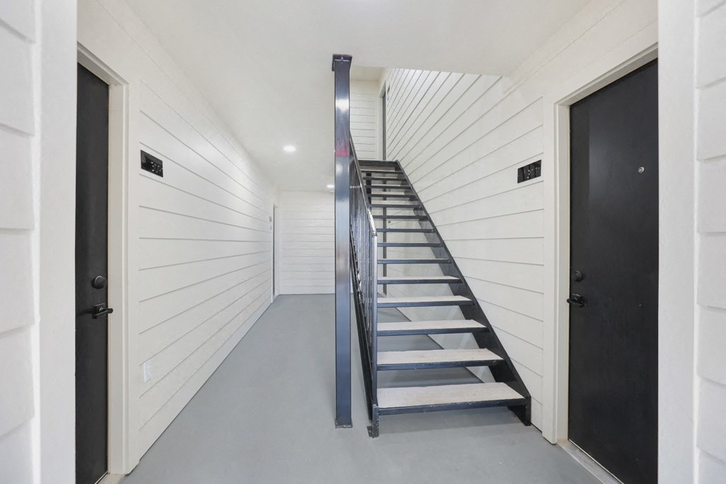 a long hallway with white walls and a staircase with a blue railing
