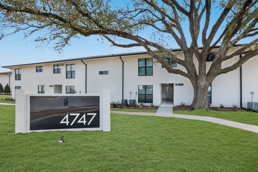 a sign in front of a white building with a large tree in the background