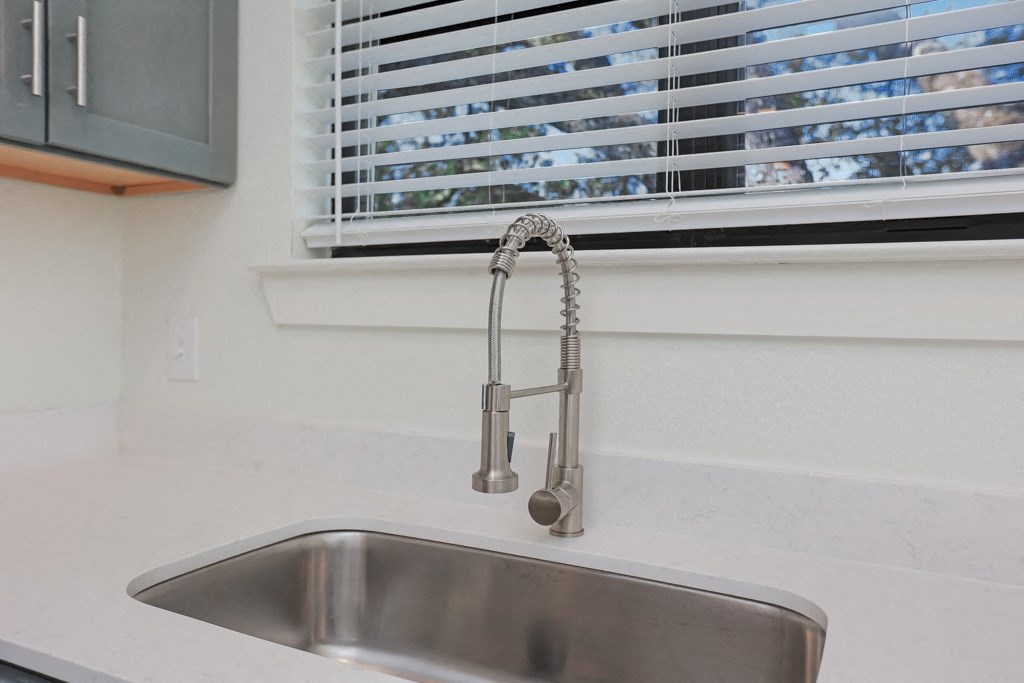 a kitchen sink in front of a window with venetian blinds