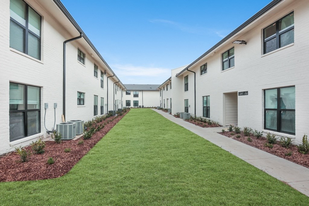 a courtyard with a green lawn and white buildings on either side