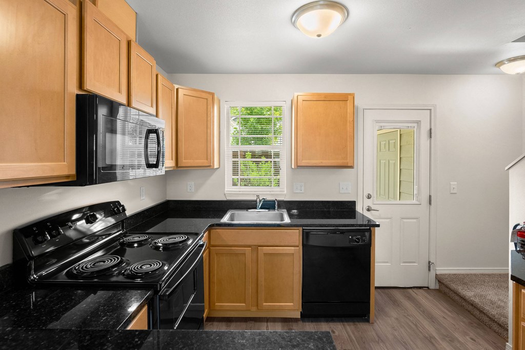 a kitchen with black counter tops and black appliances and wooden cabinets at Trillium Apartments, Springfield, OR