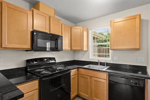a kitchen with black counters and black appliances and wooden cabinets