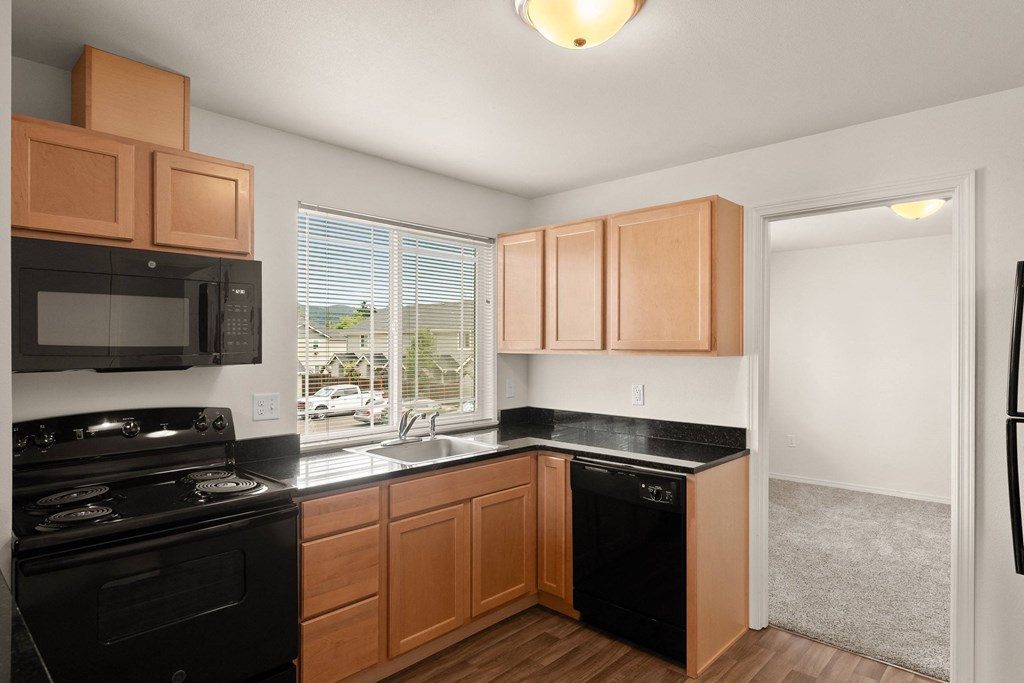 an empty kitchen with black appliances and wooden cabinets at Trillium Apartments, Springfield, OR, 97477