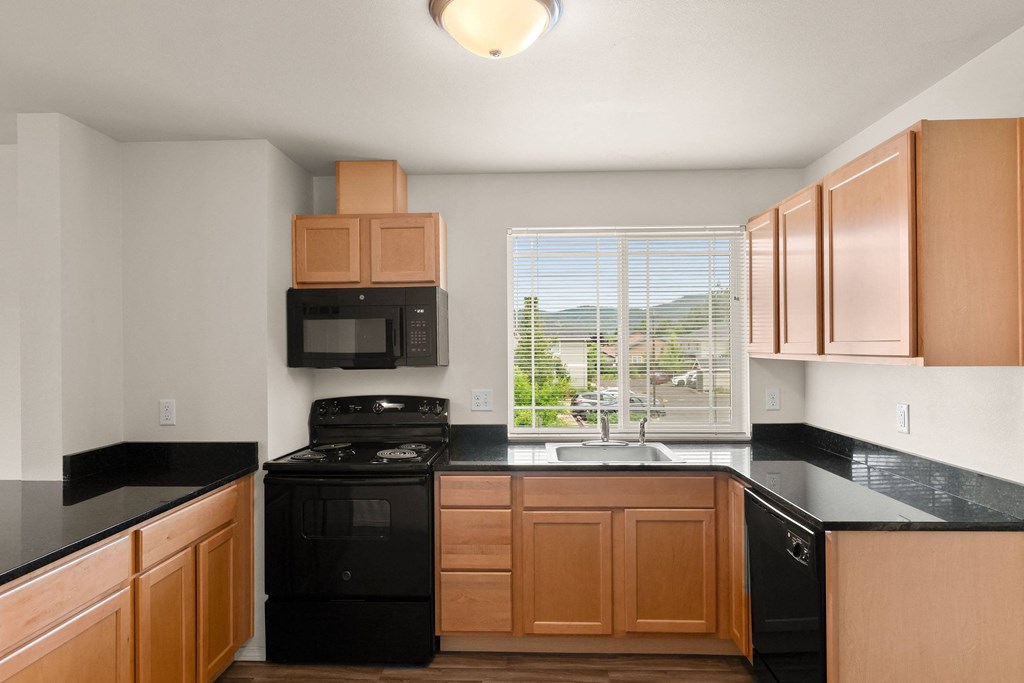 an empty kitchen with black counter tops and wooden cabinets at Trillium Apartments, Oregon 97477