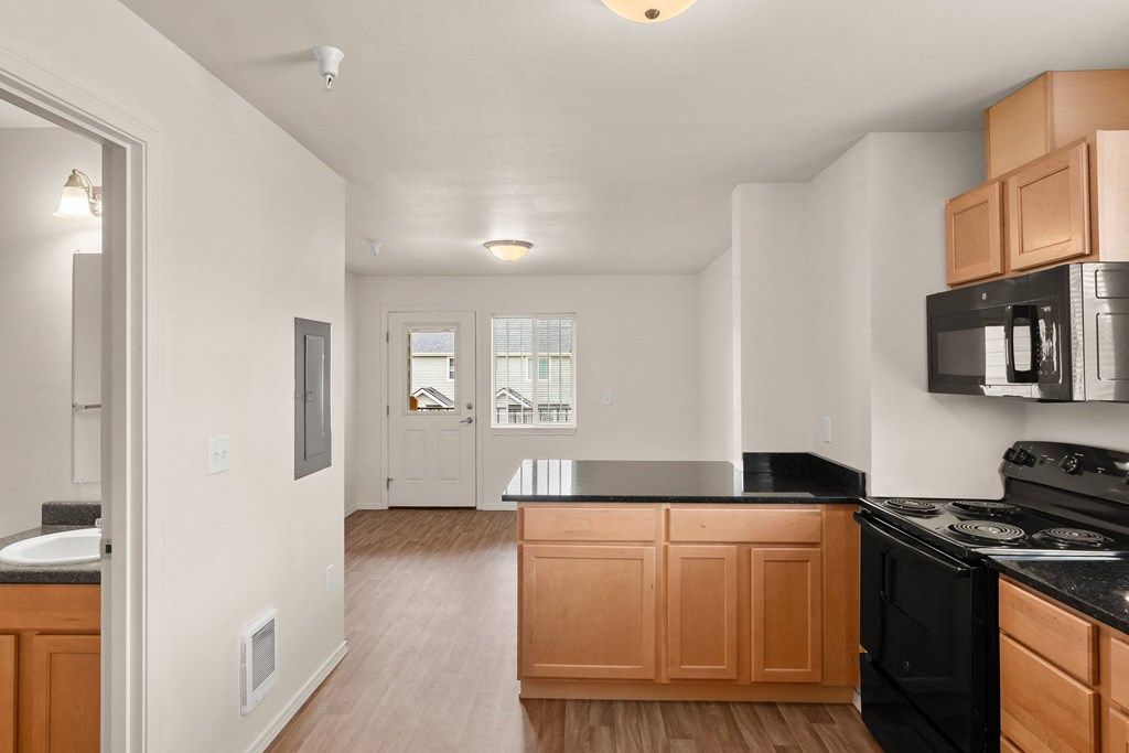 an empty kitchen with wooden cabinets and a black counter top at Trillium Apartments, Springfield