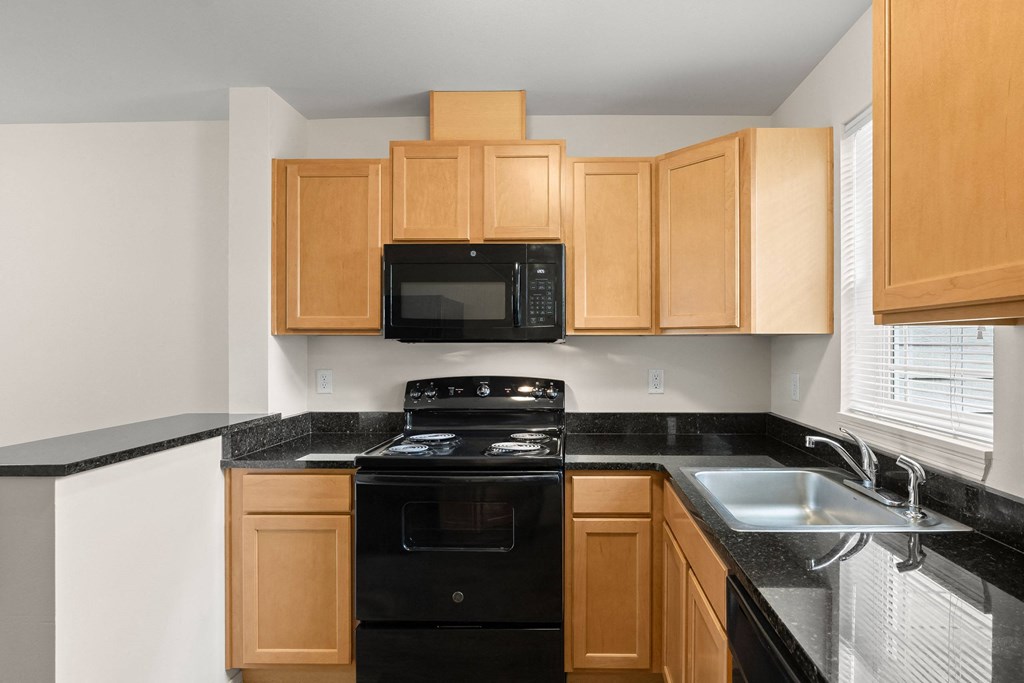 a kitchen with wood cabinets and black counter tops and black appliances at Trillium Apartments, Oregon