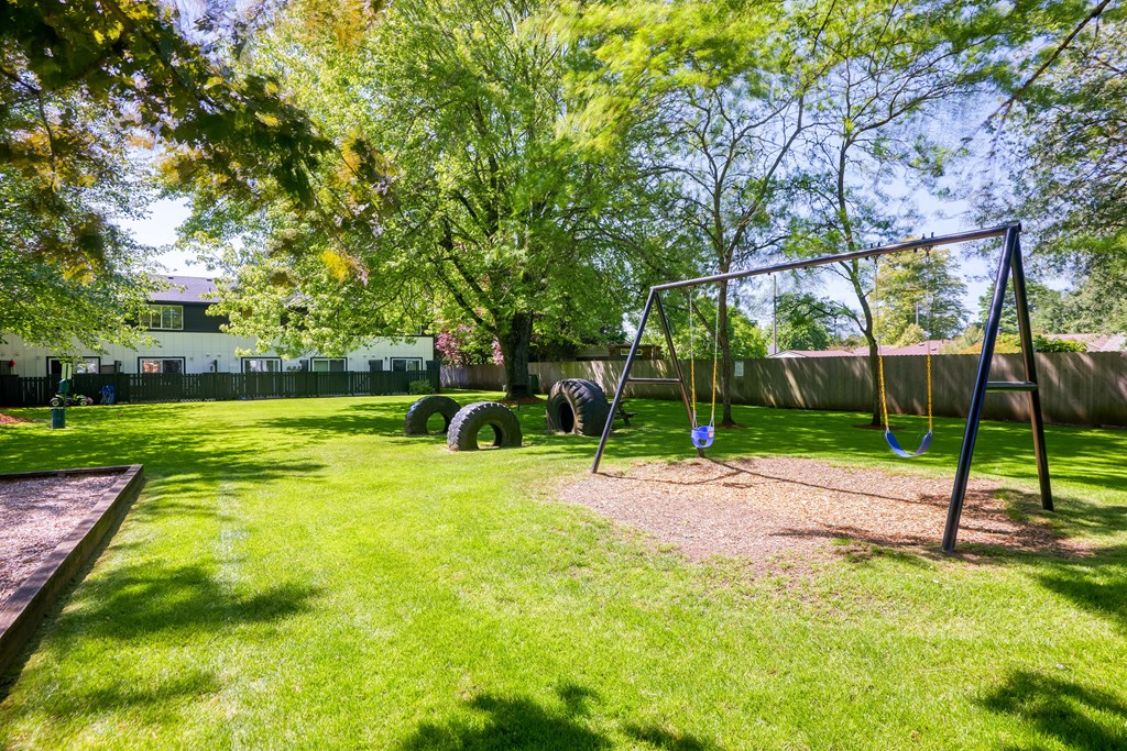 a swing set in the middle of a grassy area with trees in the background