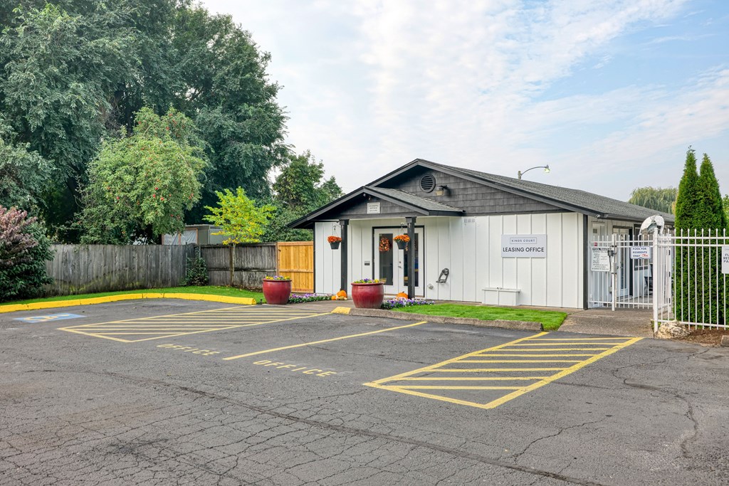 the entrance to a parking lot with a white building and a fence