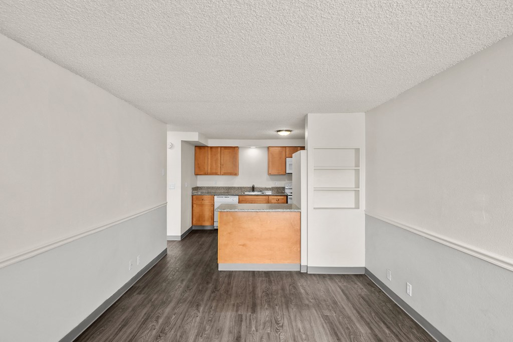 the living room and kitchen of an apartment with white walls and wood floors