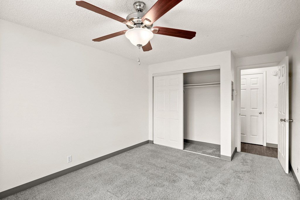 an empty living room with a ceiling fan and a closet