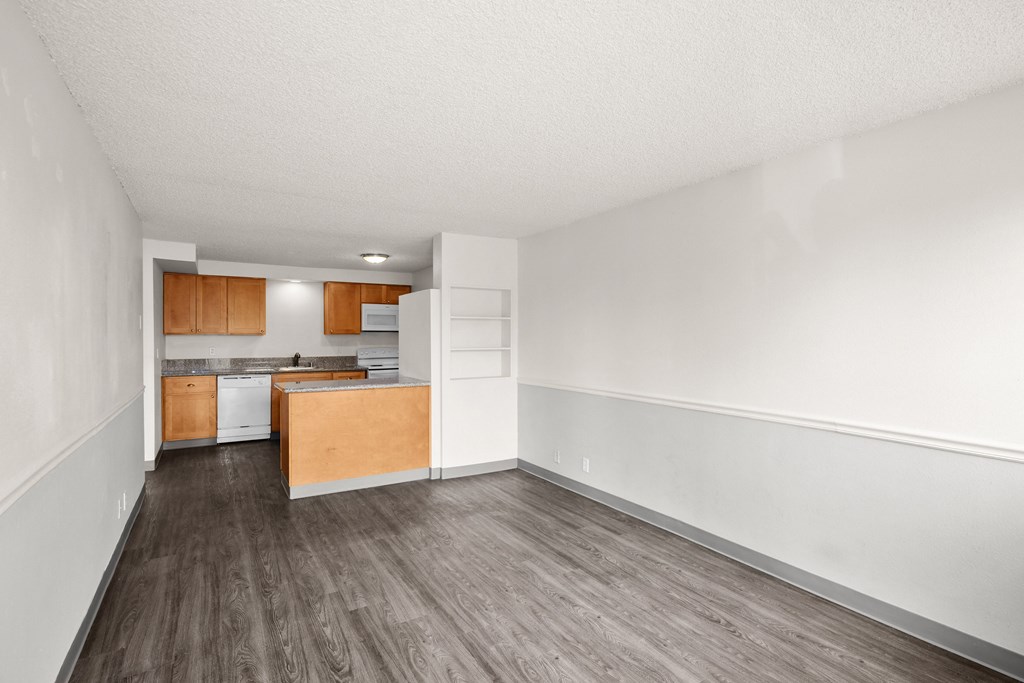 an empty living room and kitchen with wood flooring and white walls
