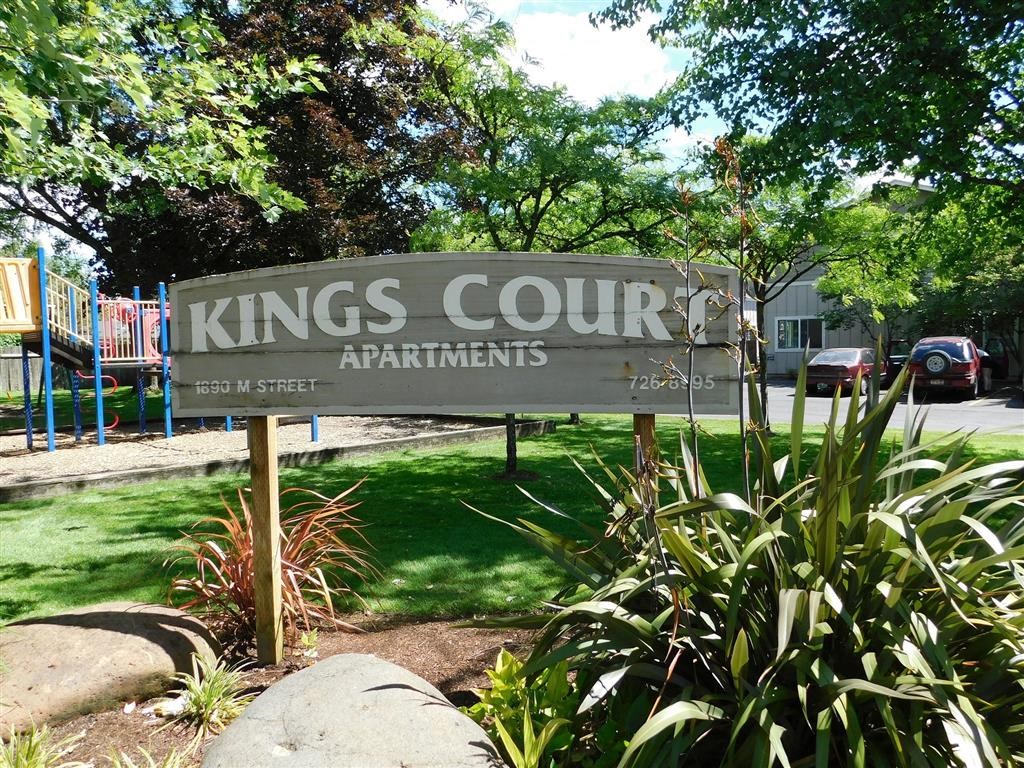 a sign for kings court apartments in front of a playground