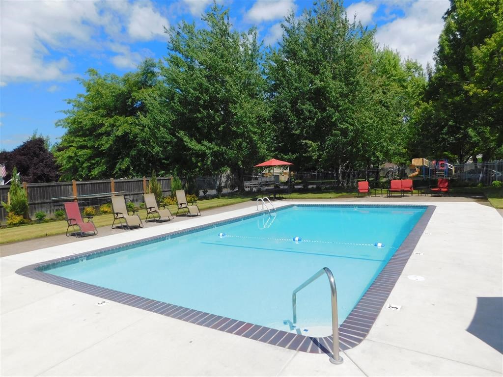 a swimming pool with chairs around it in front of trees