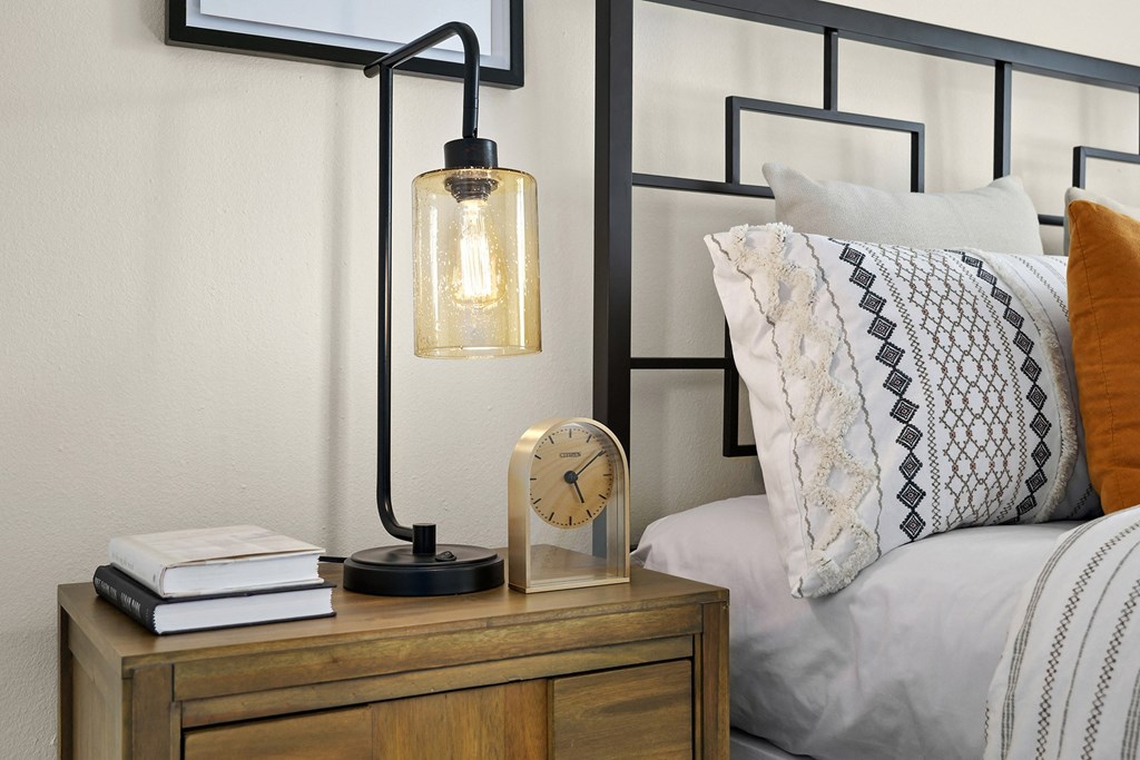 a nightstand with a clock and a lamp on it next to a bed