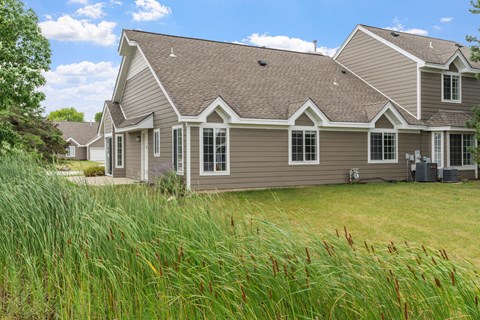 A house with a grey roof and white windows is surrounded by greenery.
