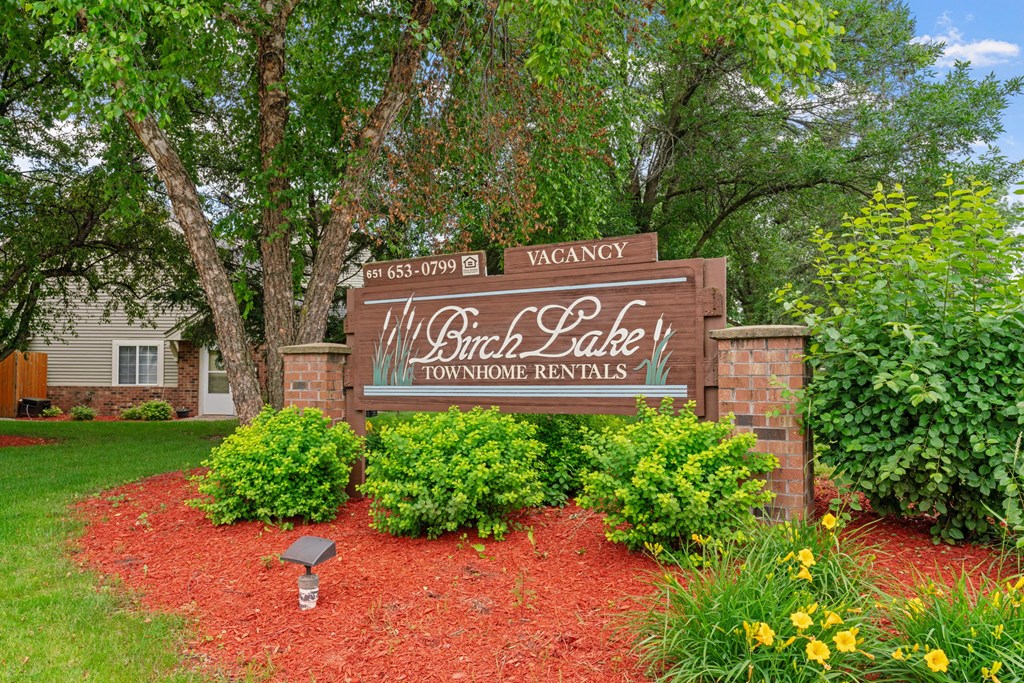 A sign for Will Branch Lake Townhomes Rentals is surrounded by greenery and flowers.