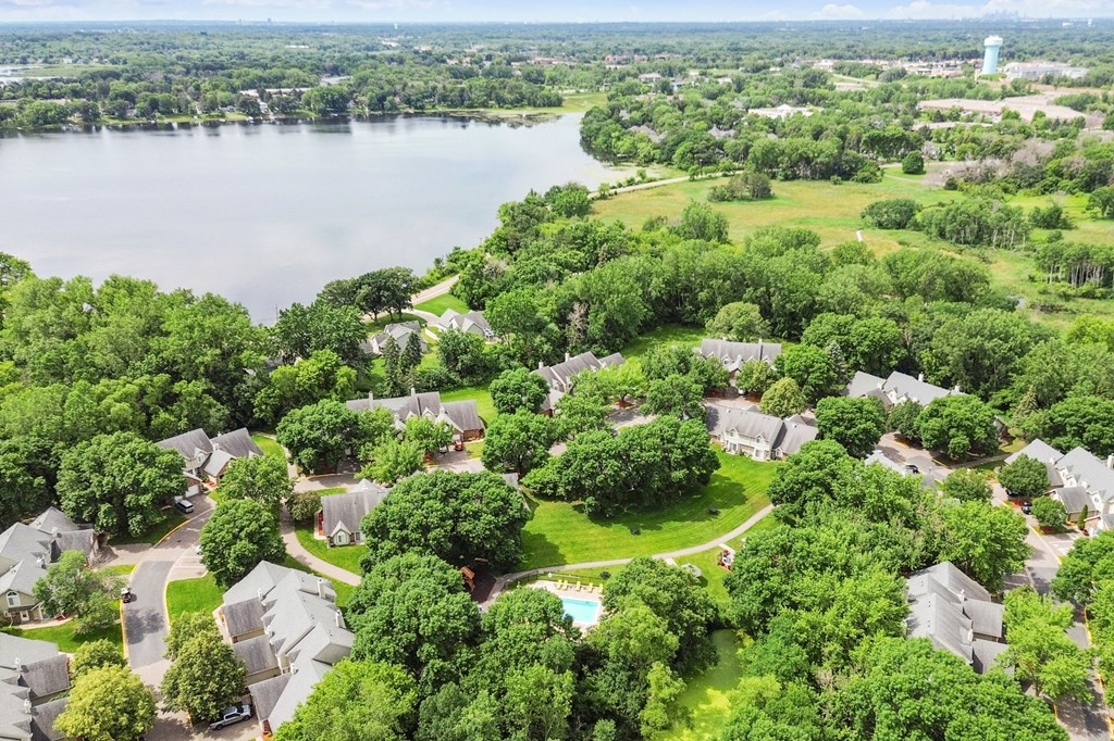 A bird's eye view of a residential area with houses surrounded by trees and a lake in the background.