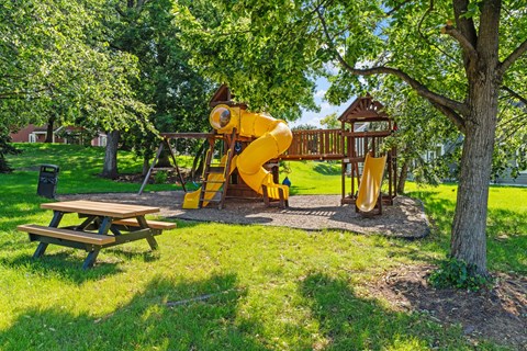 A playground with a yellow slide and a picnic table.