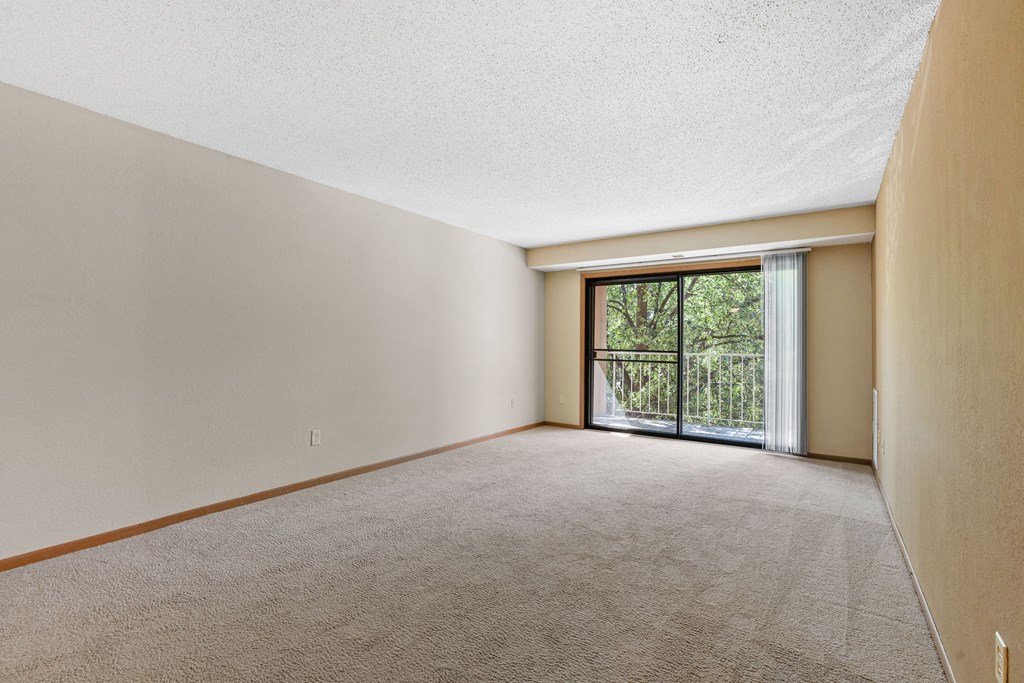 an empty living room with a sliding glass door to a balcony