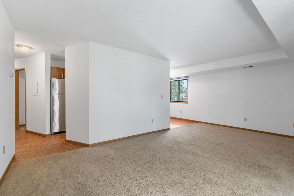 an empty living room with white walls and wood floors and a refrigerator