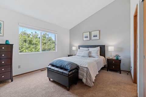 A bedroom with a bed, nightstand, and window.