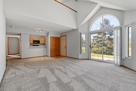 an empty living room with a large window and a door to a kitchen