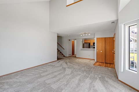 A spacious room with a carpeted floor and a staircase in the background.