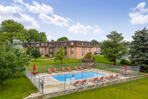A pool surrounded by a fence with red chairs.