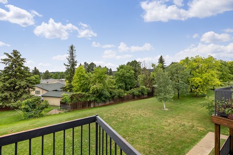 A balcony overlooks a green yard with trees.
