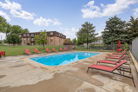 A pool surrounded by red chairs and trees.