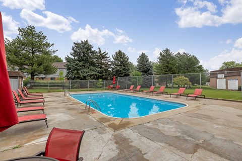 A pool surrounded by red chairs and trees.