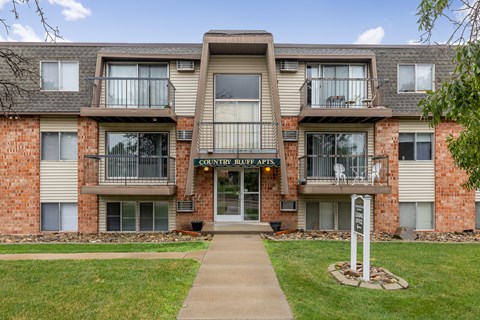 The image shows a multi-story apartment building named "Country Cuts Apartments" with a clear sky in the background.