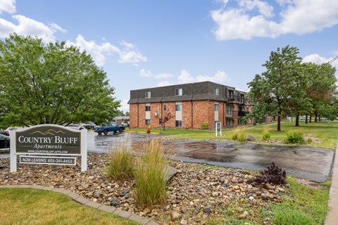 A sign for Country Bluff Apartments is in front of a brick building.