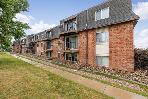 A row of red brick apartment buildings with a sidewalk in front.